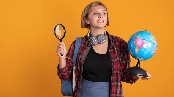 pleased-young-slavic-student-girl-with-headphones-wearing-backpack-holds-globe-magnifying-glass.jpg