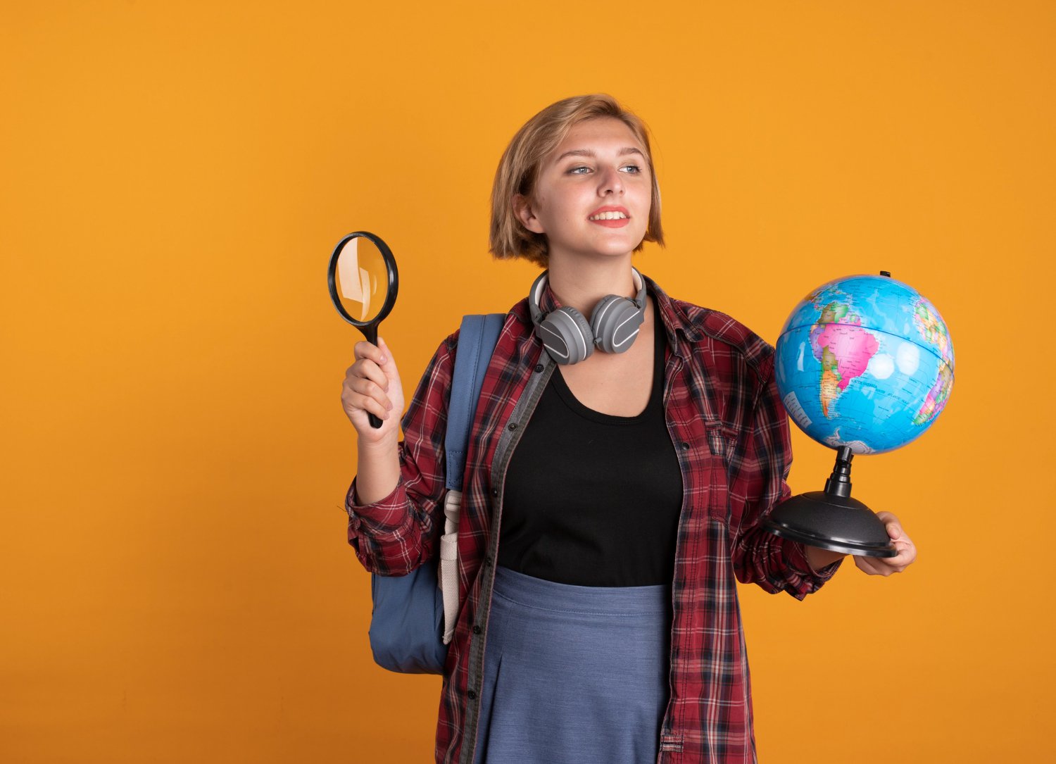 pleased-young-slavic-student-girl-with-headphones-wearing-backpack-holds-globe-magnifying-glass.jpg